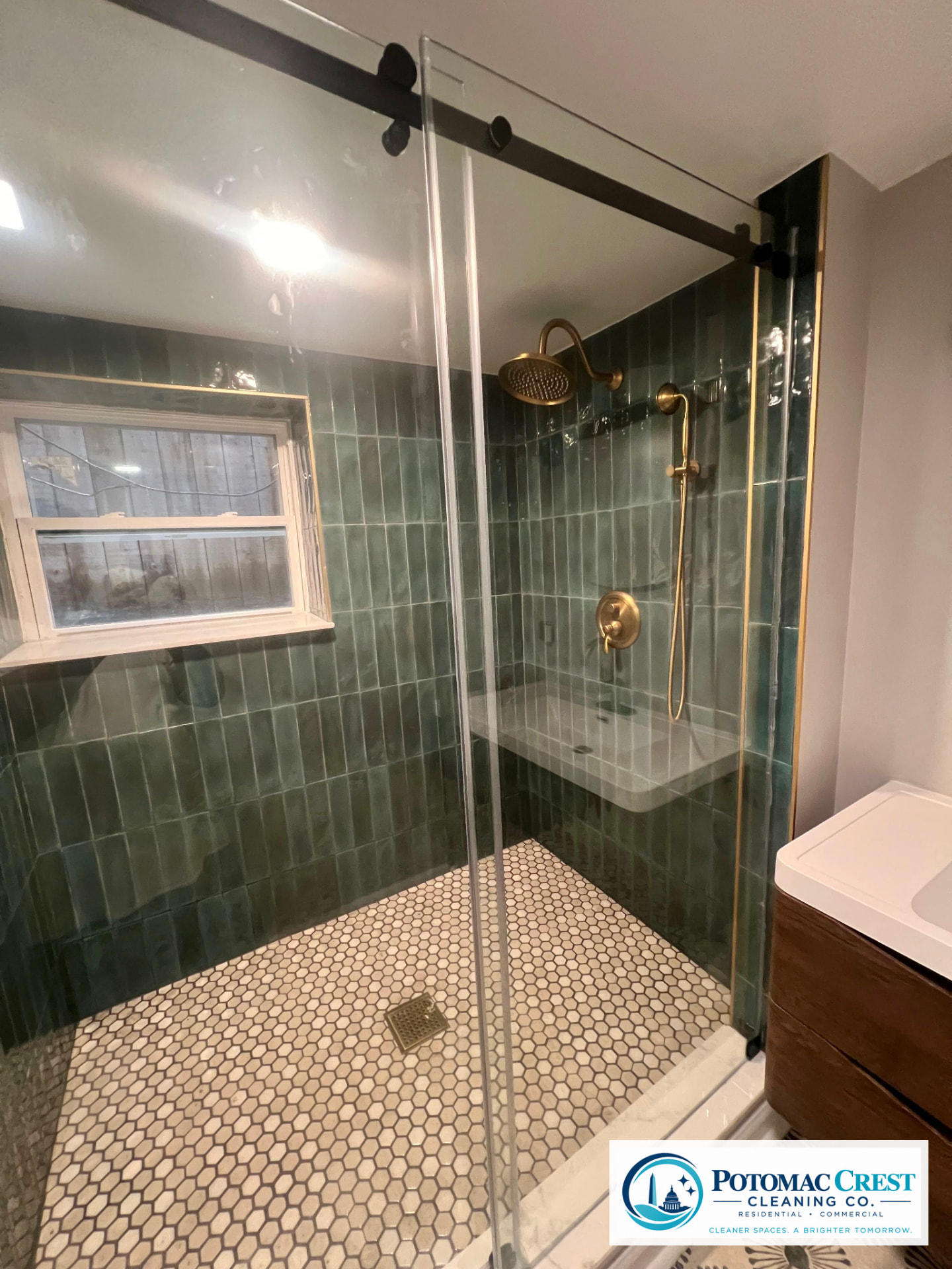 Spotless walk-in shower with green tile, brass fixtures, and clear glass door